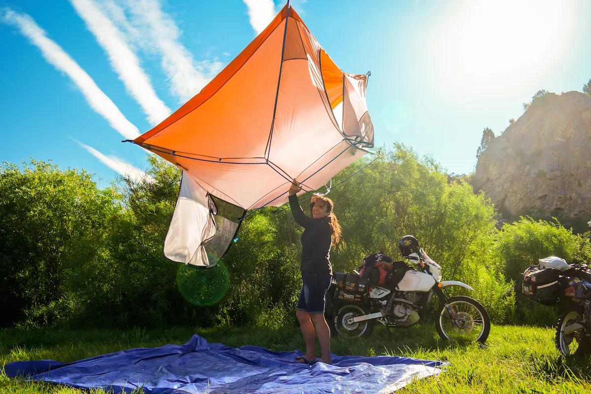 Traveller pitching a lightweight Sea to Summit tent beside adventure motorcycles while camping on an overland motorcycle trip.